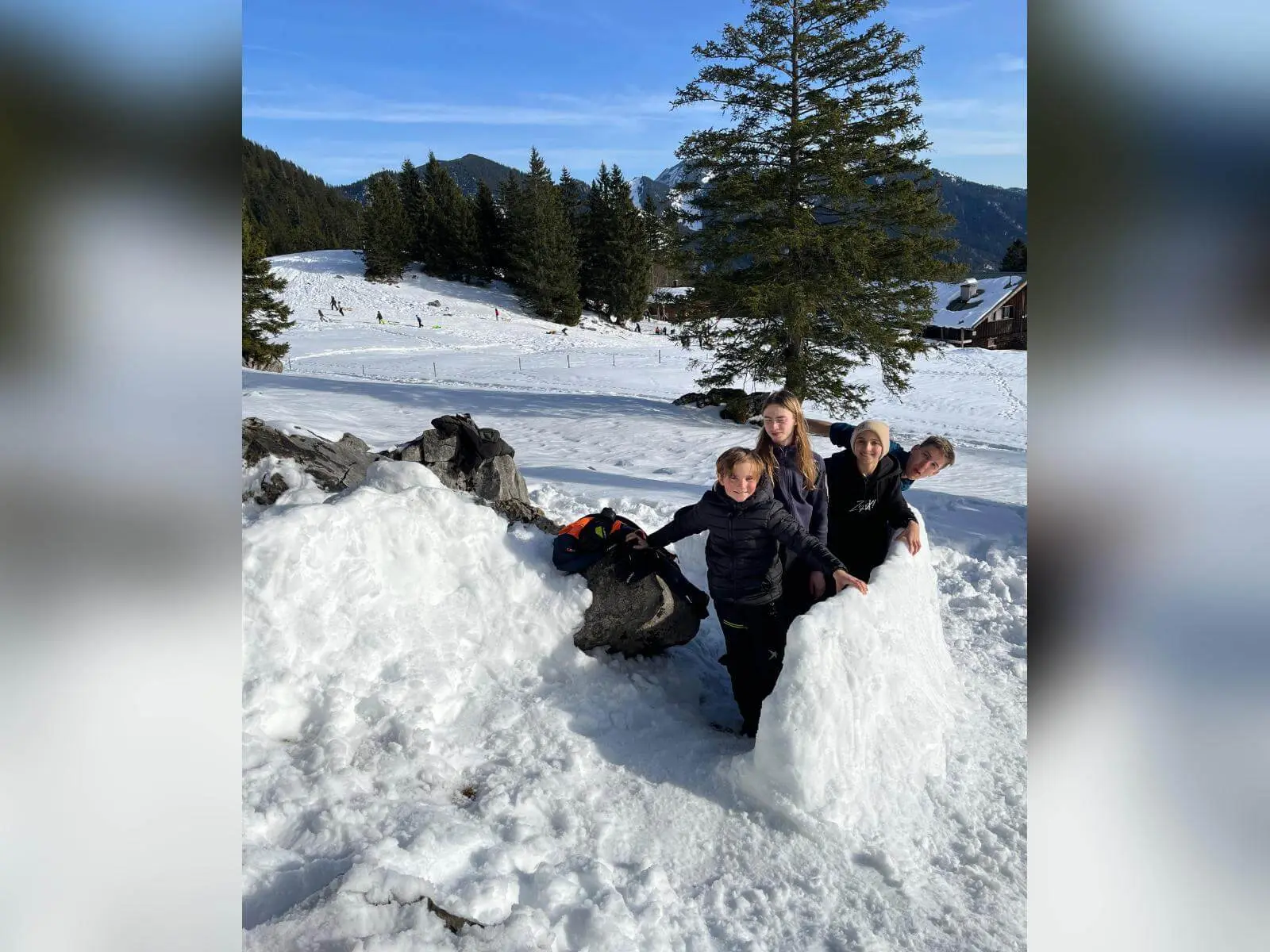 Fünf Jugendliche der Jugendgruppen Bergdohlen stehen im Schnee neben großen Schneehügeln, im Hintergrund verschneite Wiesen, Bäume und Berge bei Sonnenschein. | © DAV Markt Schwaben / Wiebke Rauschenbach