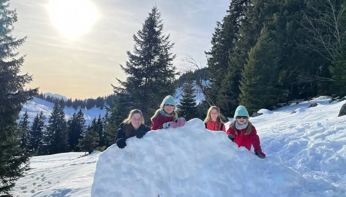 Vier Jugendliche der Jugendgruppen Bergdohlen lehnen lachend an einem großen Schneehaufen, umgeben von verschneitem Wald und Berglandschaft bei tief stehender Sonne. | © DAV Markt Schwaben / Wiebke Rauschenbach