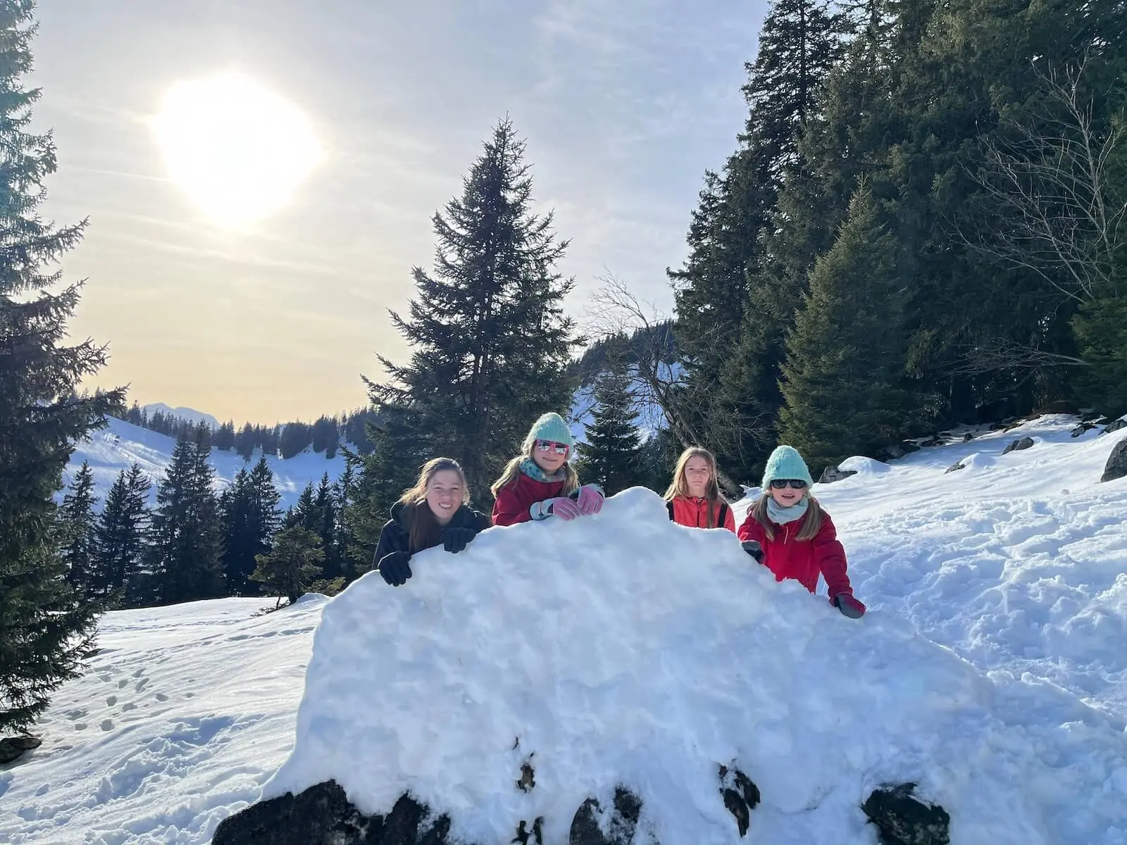 Vier Jugendliche der Jugendgruppen Bergdohlen lehnen lachend an einem großen Schneehaufen, umgeben von verschneitem Wald und Berglandschaft bei tief stehender Sonne. | © DAV Markt Schwaben / Wiebke Rauschenbach