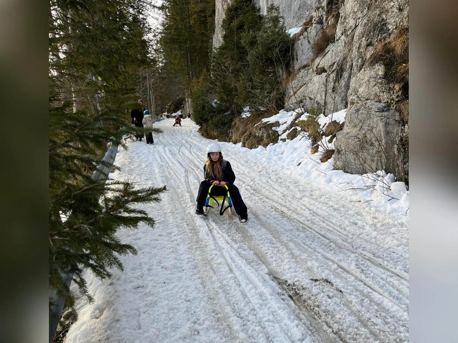 Ein Jugendlicher der Jugendgruppen Bergdohlen rodelt auf einem Winterweg durch den Wald, links Fichten, rechts eine Felswand mit Schnee. | © DAV Markt Schwaben / Wiebke Rauschenbach