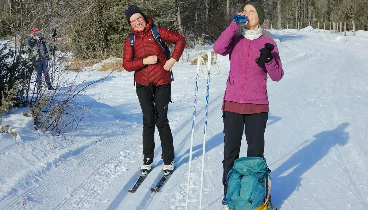 Zwei Langläufer machen auf der verschneiten Kanadaloipe eine Pause. Im Hintergrund verläuft die gespurte Strecke durch die Winterlandschaft. | © DAV Markt Schwaben/Lutz Gründel