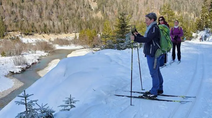 Langläufer stehen auf einer gespurten Loipe über dem winterlichen Isartal. Unterhalb schlängelt sich die Isar durch die verschneite Landschaft. | © DAV Markt Schwaben/Lutz Gründel
