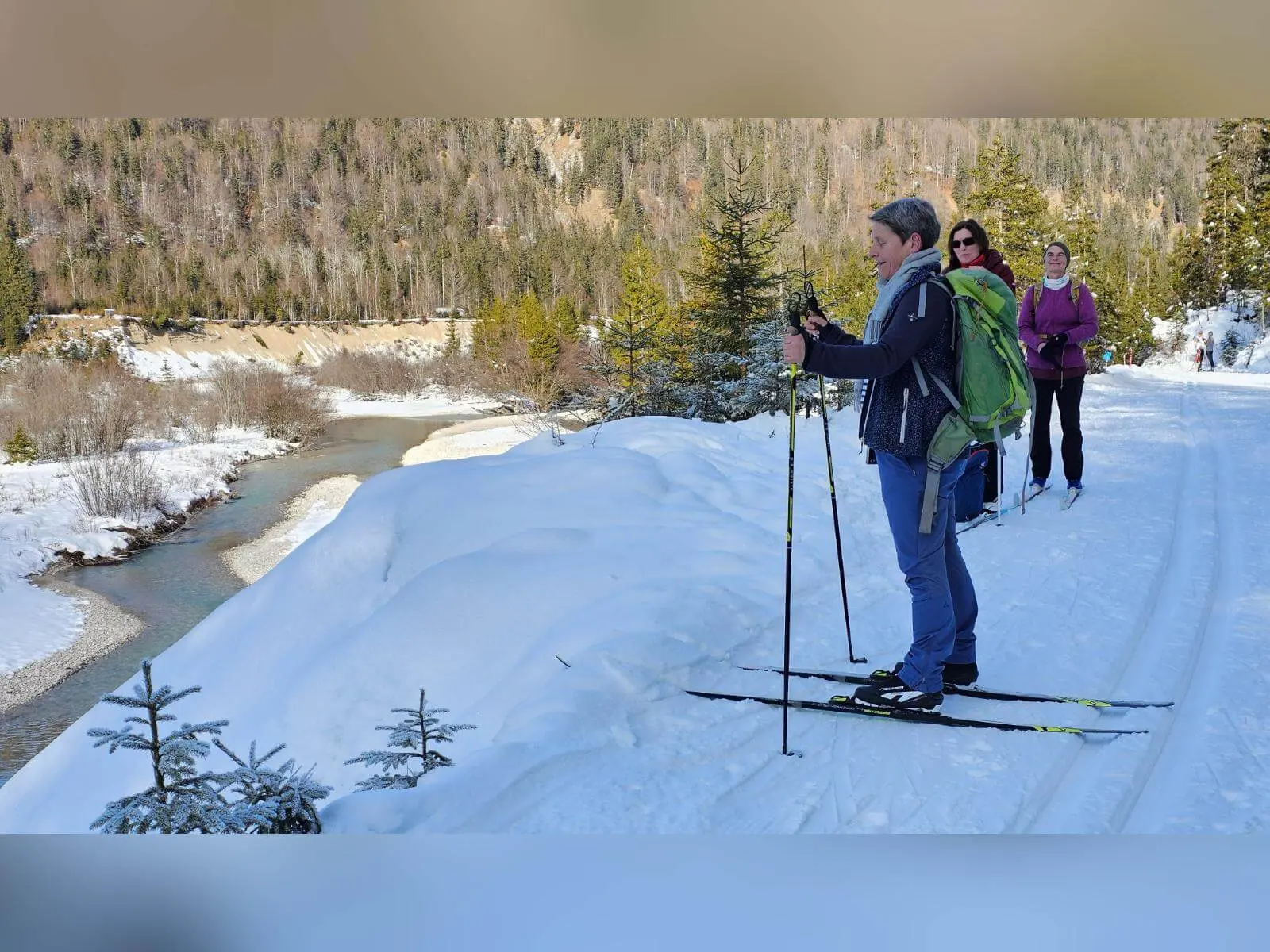 Langläufer stehen auf einer gespurten Loipe über dem winterlichen Isartal. Unterhalb schlängelt sich die Isar durch die verschneite Landschaft. | © DAV Markt Schwaben/Lutz Gründel