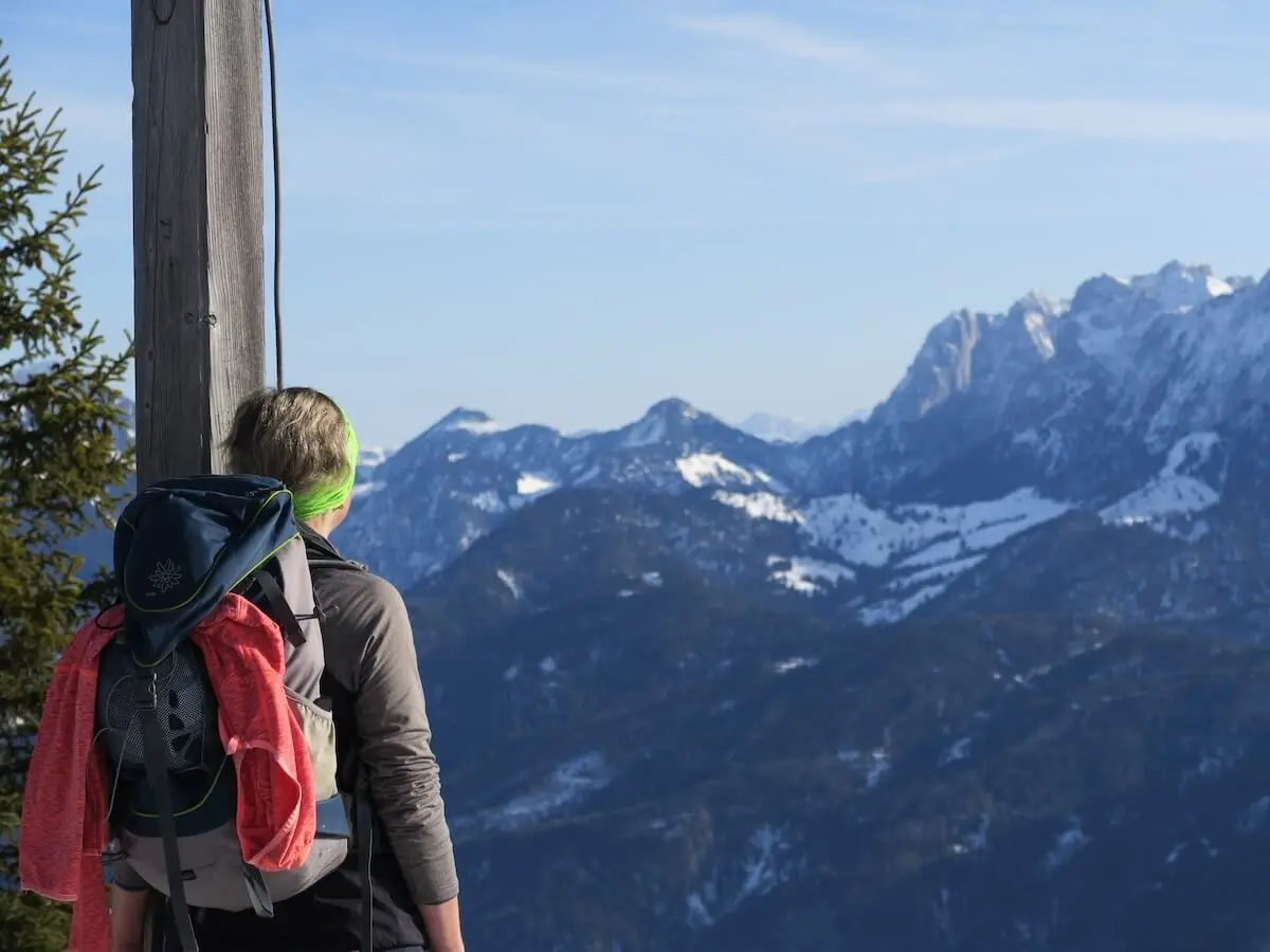 Eine Person steht mit Rucksack am verschneiten Bergpfad neben einem Holzpfosten und schaut über die weiten, klaren Alpen mit schneebedeckten Gipfeln. | © DAV Markt Schwaben / Erwin Matzinger