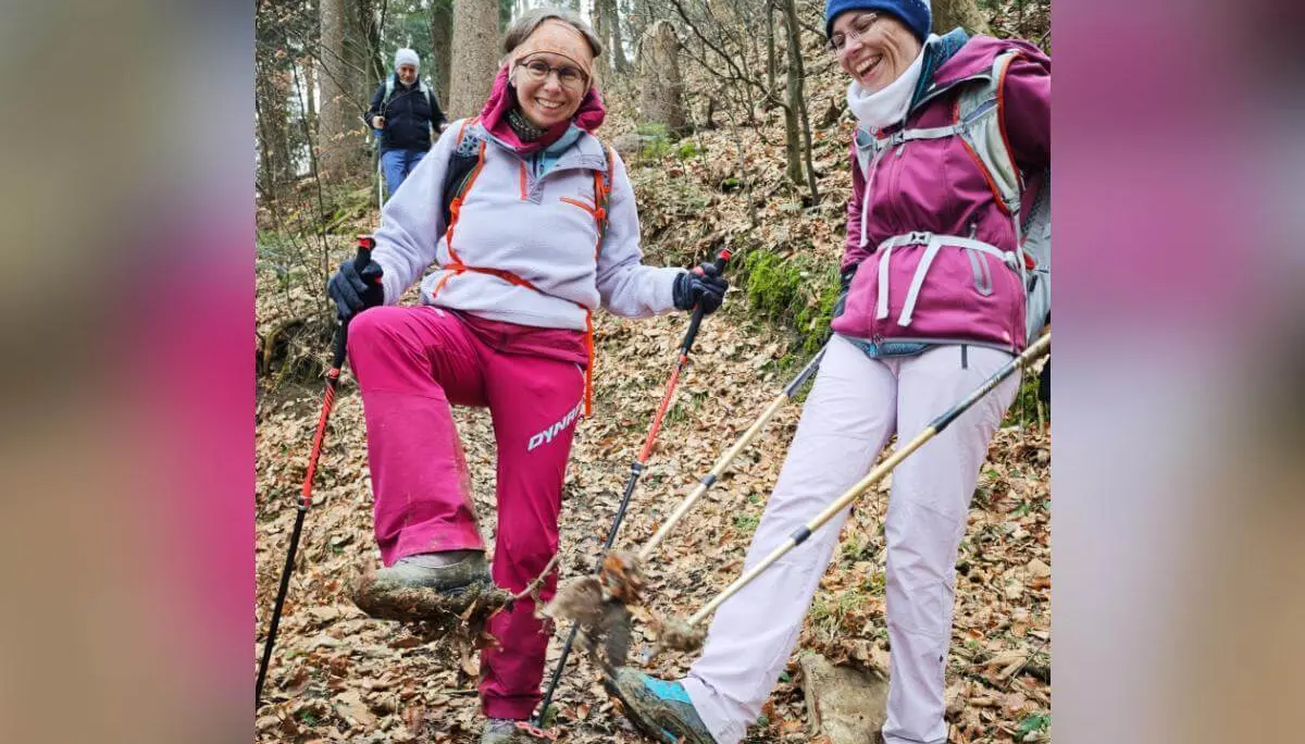 Zwei Wandernde stehen lachend auf einem laubbedeckten Waldweg; eine Person zeigt ihren stark verschmutzten Schuh, hinten folgt ein weiterer Wanderer. | © DAV Markt Schwaben/Erwin Matzinger