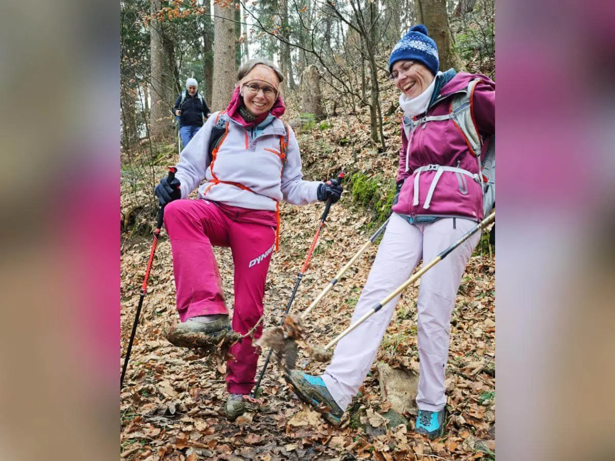 Zwei Wandernde stehen lachend auf einem laubbedeckten Waldweg; eine Person zeigt ihren stark verschmutzten Schuh, hinten folgt ein weiterer Wanderer. | © DAV Markt Schwaben/Erwin Matzinger