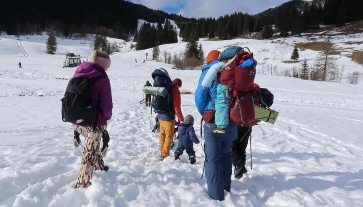 Eine Gruppe aus Kindern und Erwachsenen wandert durch verschneites Gelände bergauf; sie tragen Winterkleidung und Rucksäcke, umgeben von Wald und Hügeln. | © DAV Markt Schwaben