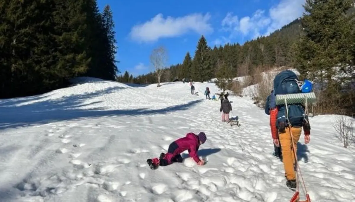 Mehrere Menschen steigen durch verschneites Gelände bergauf; vorn zieht eine Person einen Schlitten, andere folgen mit Hunden und Rucksäcken unter blauem Himmel. | © DAV Markt Schwaben
