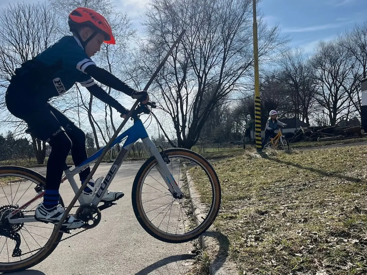 Ein Kind fährt im Vordergrund auf einem weiß‑blauen Mountainbike, während ein weiteres Kind im Hintergrund auf einem gelben Rad neben einem markierten Pfosten unterwegs ist. | © DAV Markt Schwaben/Miron Thoms