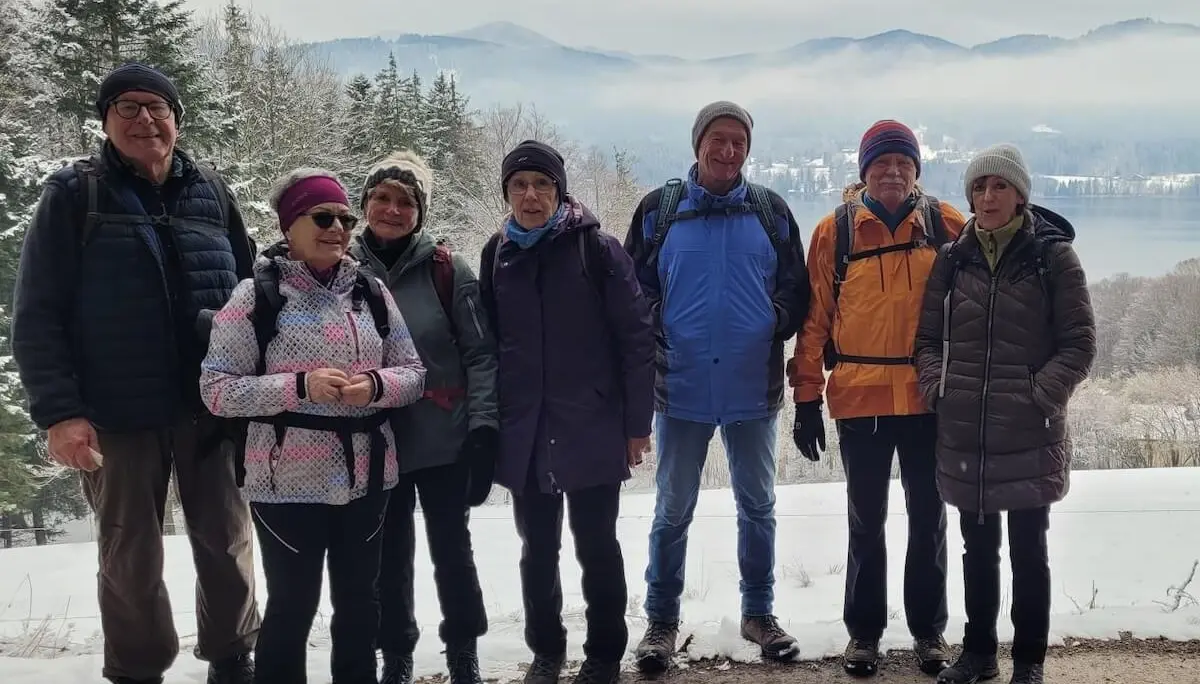 Acht Wandernde stehen auf einem verschneiten Weg; vorne die Gruppe, dahinter See, Bäume und nebelige Berge in winterlicher Landschaft. | © DAV Markt Schwaben/Hubert Inhofer
