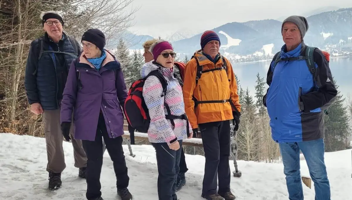 Sechs Wandernde stehen auf einem verschneiten Weg; vorne die Gruppe, dahinter ein See, schneebedeckte Bäume und Berge in winterlicher Weite. | © DAV Markt Schwaben/Hubert Inhofer