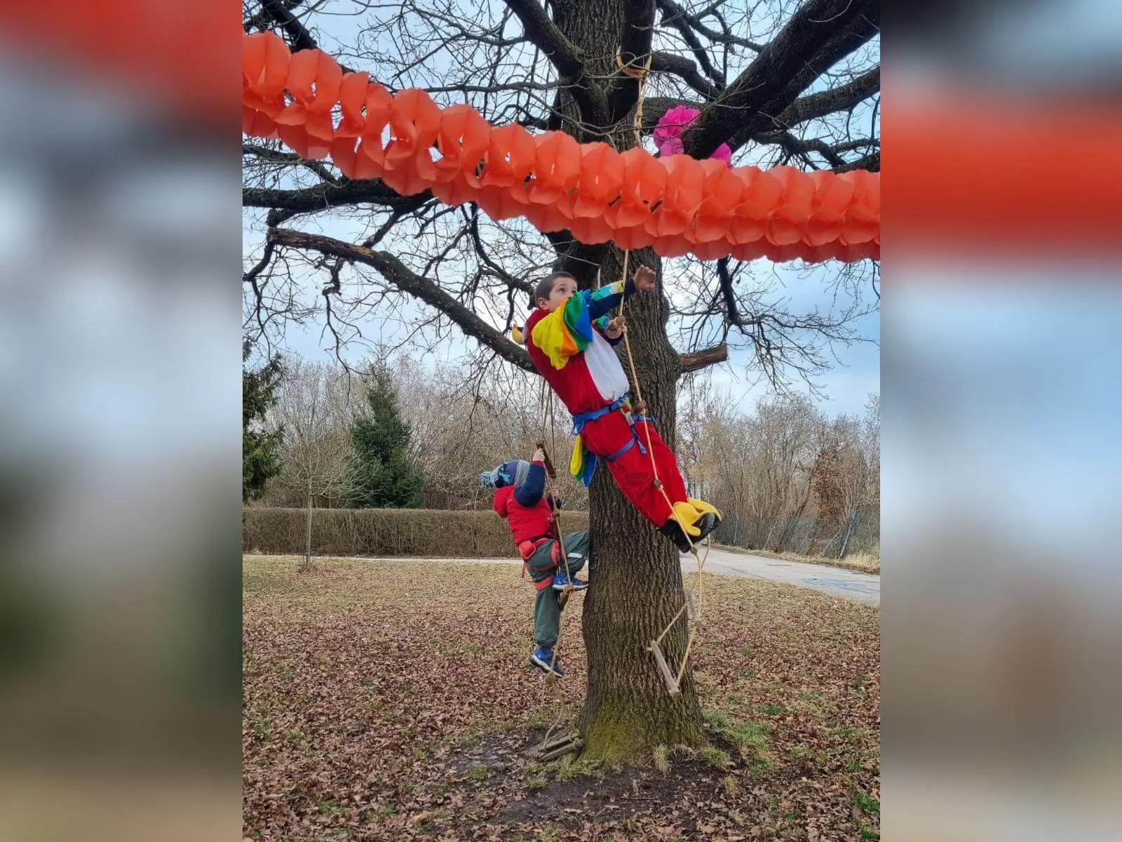 Verkleidete Kinder sichern sich beim Klettern an einem Baum, darüber orange Girlanden, winterliche Umgebung im Hintergrund. | © DAV Markt Schwaben