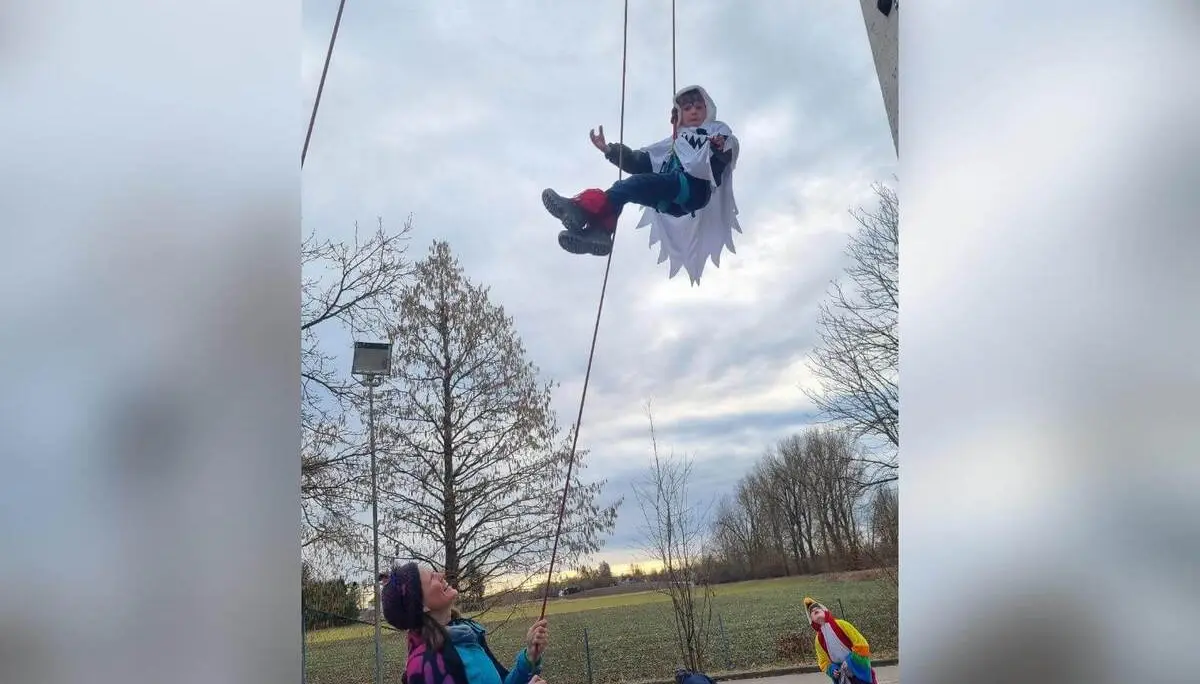 Ein verkleidetes Kind hängt gesichert an einem Kletterseil in der Luft, unten sichern Erwachsene und Kinder in bunten Kostümen. | © DAV Markt Schwaben