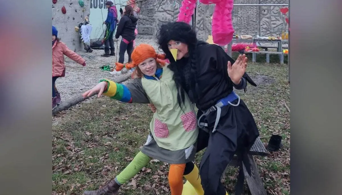 Zwei verkleidete Personen posieren lachend vor dem Kletterturm, im Hintergrund klettern Kinder und bunte Faschingsdeko hängt. | © DAV Markt Schwaben