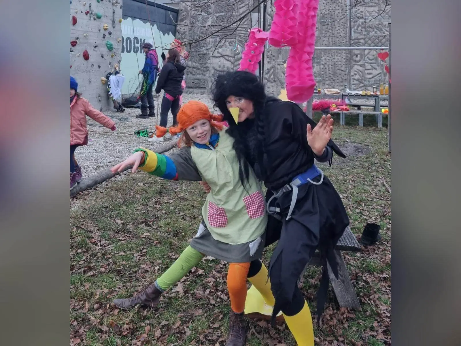 Zwei verkleidete Personen posieren lachend vor dem Kletterturm, im Hintergrund klettern Kinder und bunte Faschingsdeko hängt. | © DAV Markt Schwaben