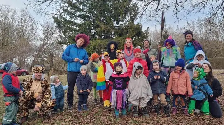 Eine große Gruppe verkleideter Kinder und Erwachsener steht gemeinsam auf einer Wiese, bunt kostümiert vor Bäumen beim Faschingsklettern. | © DAV Markt Schwaben