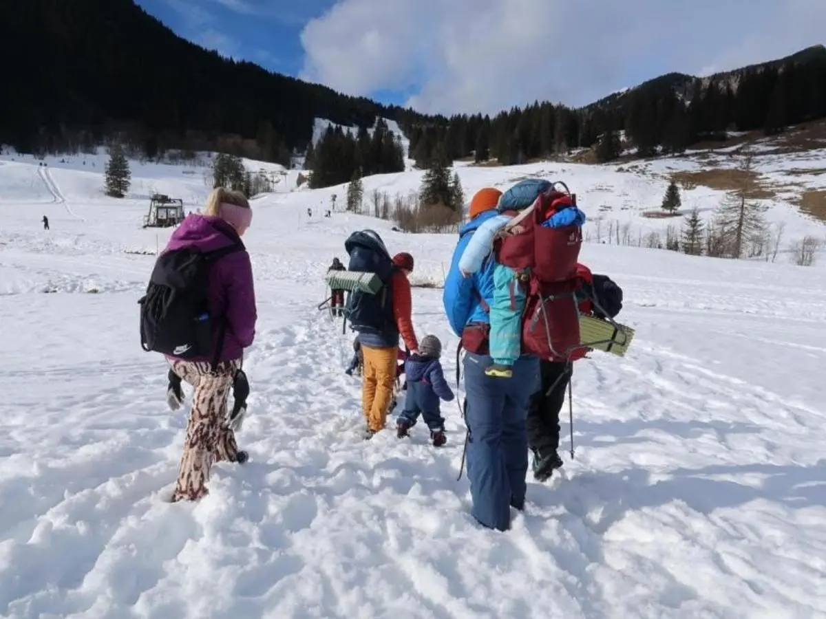 Eine Gruppe aus Kindern und Erwachsenen wandert durch verschneites Gelände bergauf; sie tragen Winterkleidung und Rucksäcke, umgeben von Wald und Hügeln. | © DAV Markt Schwaben, Familiengruppe