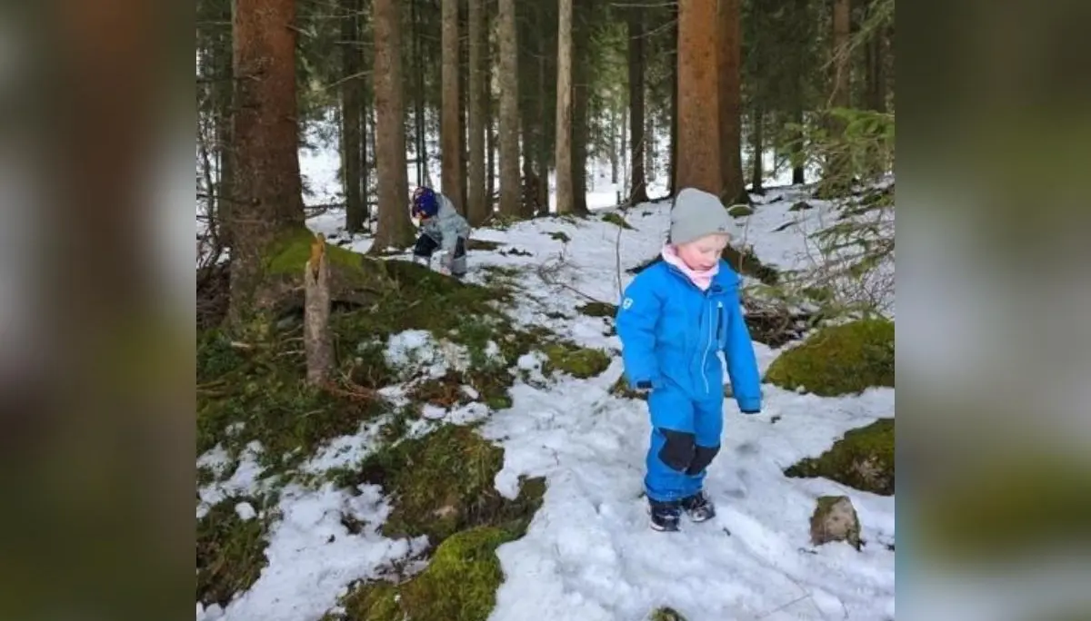 Zwei Kinder erkunden einen verschneiten Wald; vorn geht ein Kind über Schnee und Moos, hinten hockt ein weiteres zwischen den Bäumen am Aussichtsplatz. | © DAV Markt Schwaben, Familiengruppe