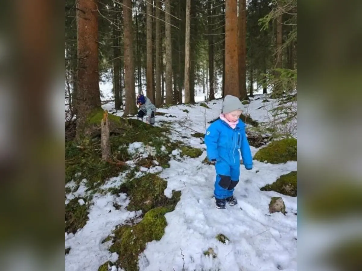 Zwei Kinder erkunden einen verschneiten Wald; vorn geht ein Kind über Schnee und Moos, hinten hockt ein weiteres zwischen den Bäumen am Aussichtsplatz. | © DAV Markt Schwaben, Familiengruppe