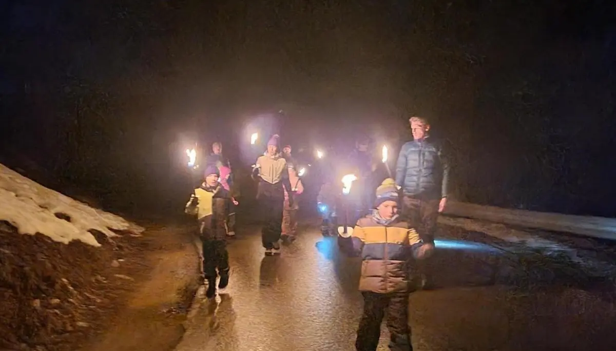 Kinder und Erwachsene gehen im Dunkeln mit brennenden Fackeln eine nasse Straße entlang; seitlich liegt Schnee, die Gruppe wirkt konzentriert und ruhig. | © DAV Markt Schwaben, Familiengruppe
