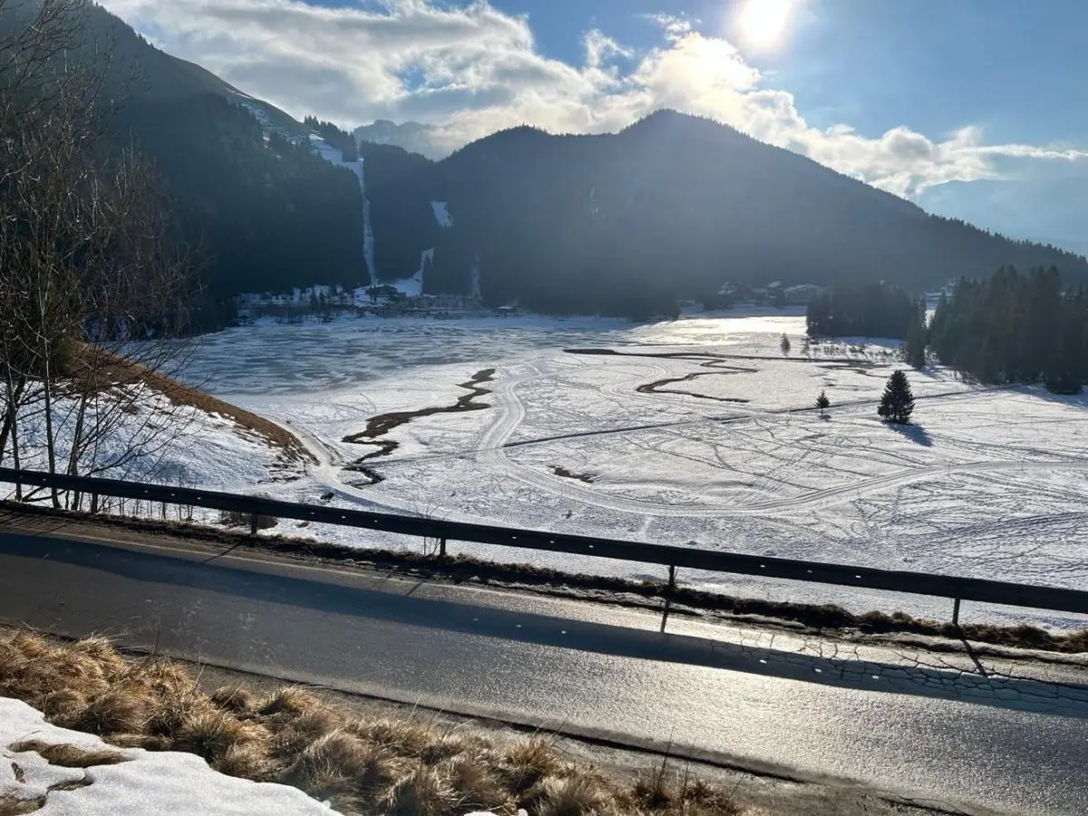 Sonnige Winterlandschaft mit gefrorenem See, verschneiten Hängen und Wald; Spuren im Schnee führen über die offene Fläche Richtung Berge. | © DAV Markt Schwaben, Familiengruppe