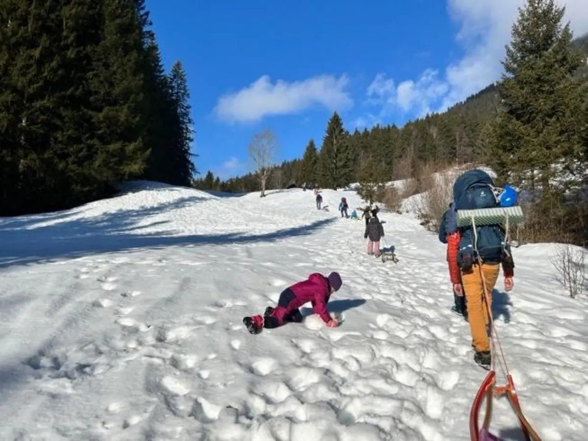 Mehrere Menschen steigen durch verschneites Gelände bergauf; vorn zieht eine Person einen Schlitten, andere folgen mit Hunden und Rucksäcken unter blauem Himmel. | © DAV Markt Schwaben, Familiengruppe