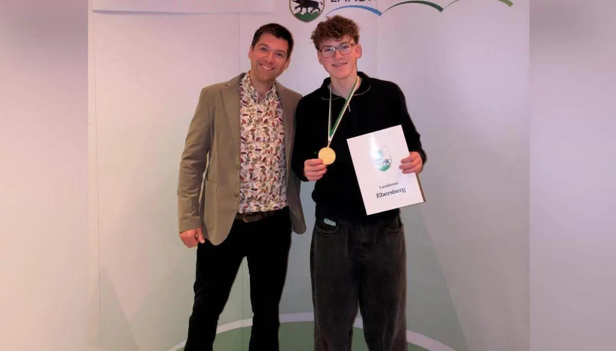 Zwei Personen stehen vor einem Banner mit der Aufschrift ‚Sportlerehrung Landkreis Ebersberg‘. Die geehrte Person trägt eine Goldmedaille um den Hals und hält eine Urkunde in den Händen.  | © Sportlerehrung Landkreis Ebersberg