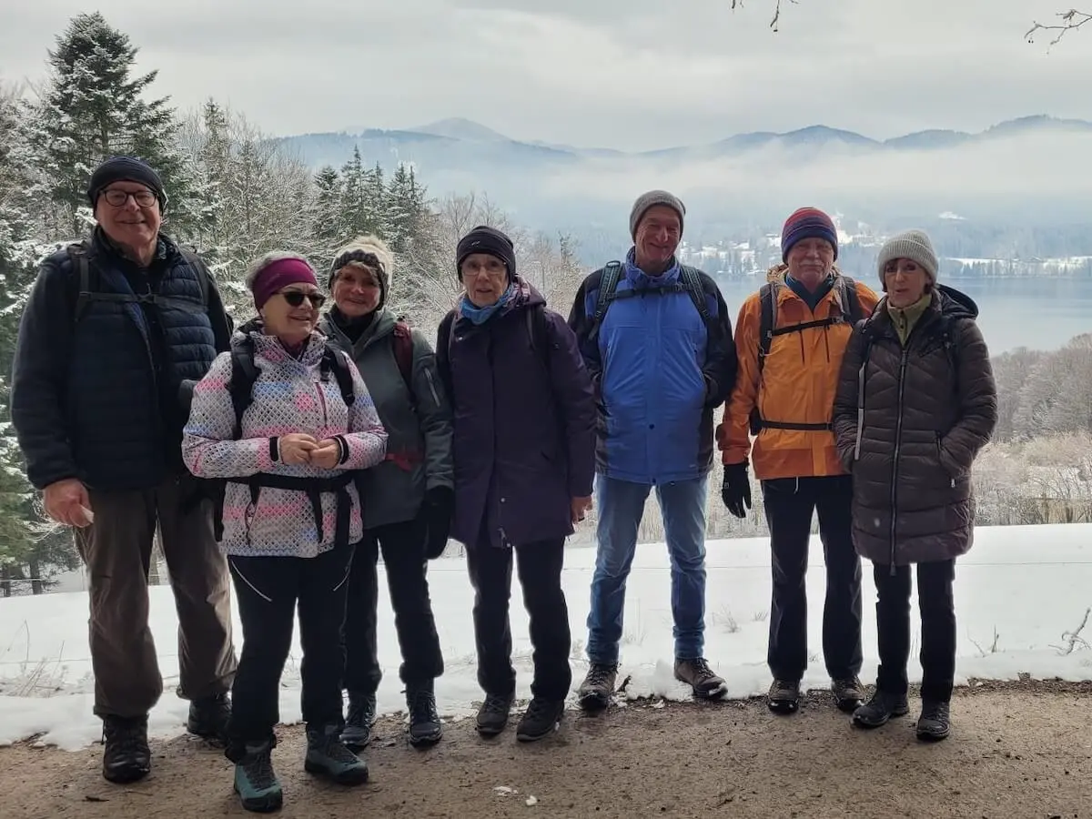 Acht Wandernde stehen auf einem verschneiten Weg; vorne die Gruppe, dahinter See, Bäume und nebelige Berge in winterlicher Landschaft. | © DAV Markt Schwaben / Hubert Inhofer