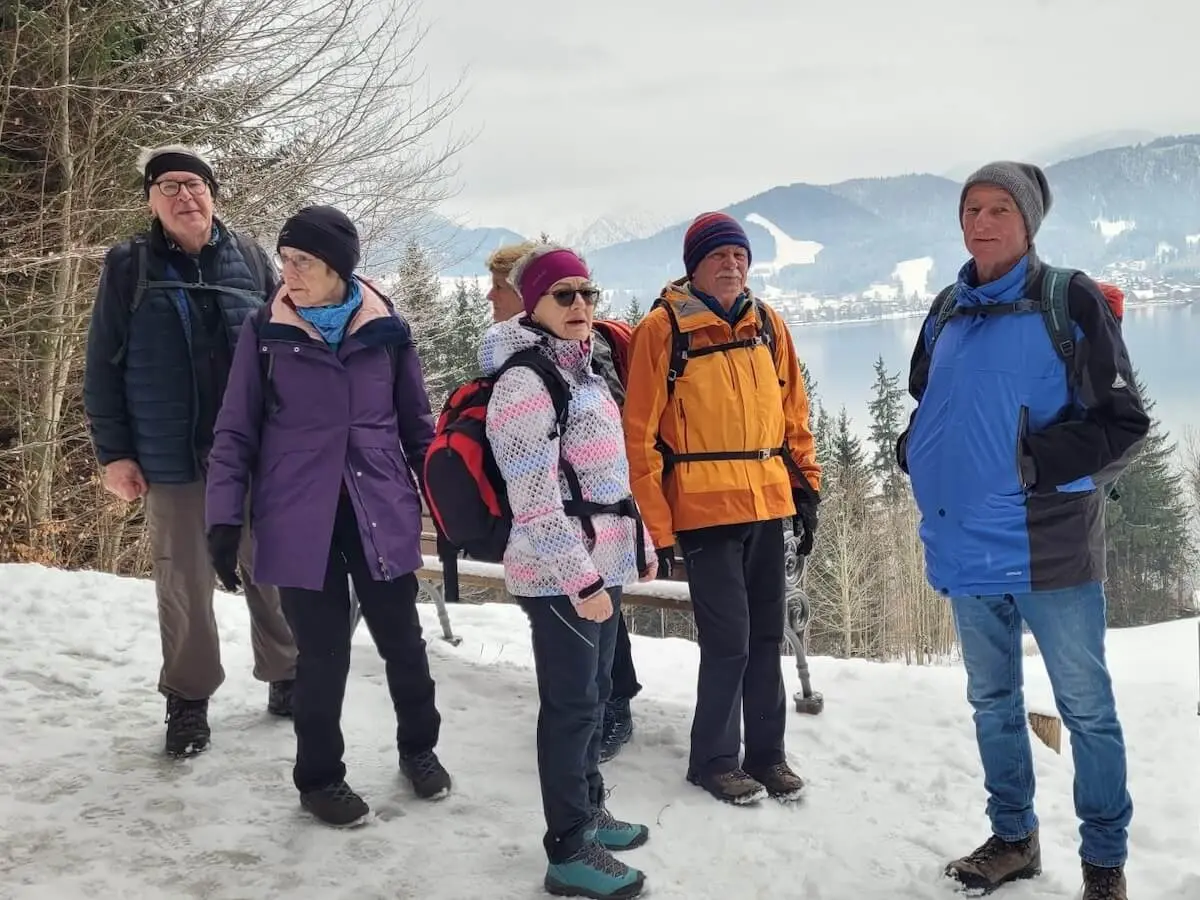 Sechs Wandernde stehen auf einem verschneiten Weg; vorne die Gruppe, dahinter ein See, schneebedeckte Bäume und Berge in winterlicher Weite. | © DAV Markt Schwaben / Hubert Inhofer