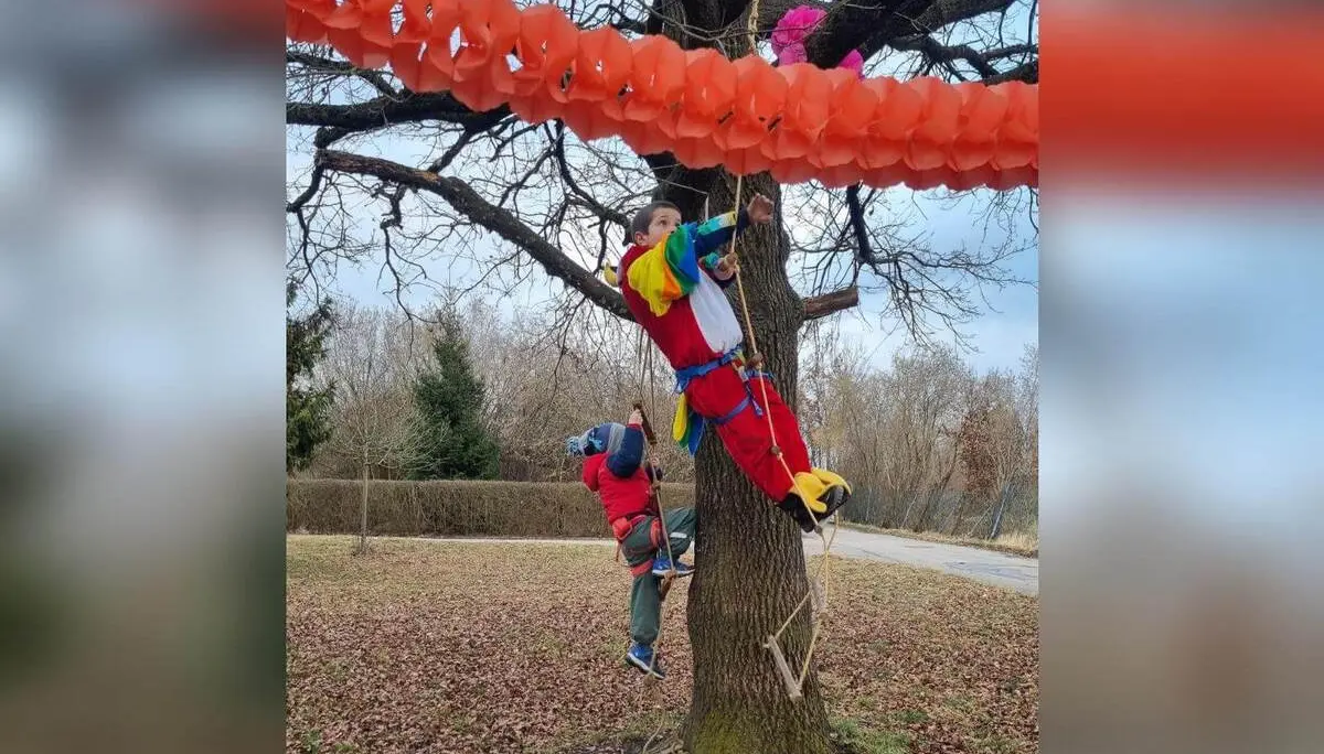 Verkleidete Kinder sichern sich beim Klettern an einem Baum, darüber orange Girlanden, winterliche Umgebung im Hintergrund. | © DAV Markt Schwaben