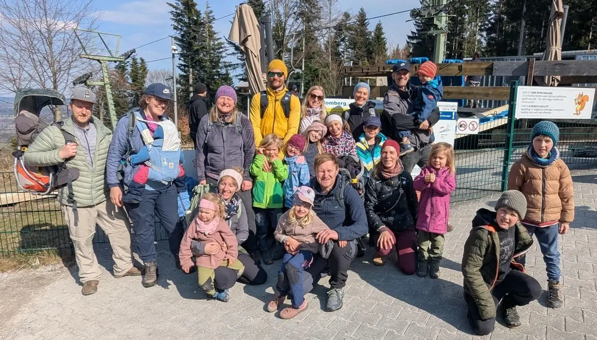 Mehrere Erwachsene und Kinder stehen vor der Blombergbahn, tragen Outdoor‑Kleidung und posieren gemeinsam für ein Gruppenfoto. | © DAV Markt Schwaben/Silke Titze