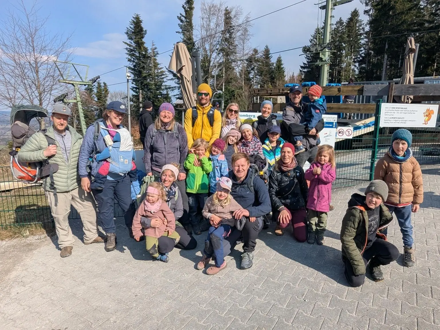 Mehrere Erwachsene und Kinder stehen vor der Blombergbahn, tragen Outdoor‑Kleidung und posieren gemeinsam für ein Gruppenfoto. | © DAV Markt Schwaben/Silke Titze