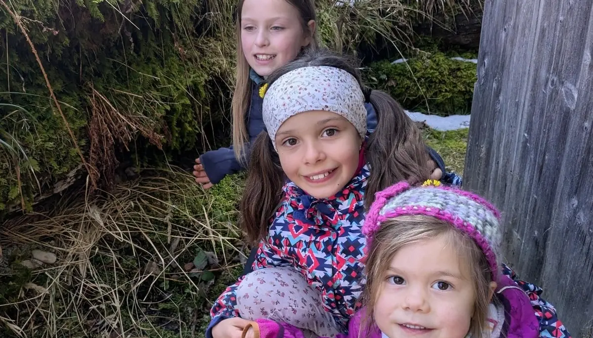 Drei Kinder hocken in winterlicher Waldumgebung auf dem Boden und betrachten etwas im Moos zwischen Gras und Schneeresten. | © DAV Markt Schwaben/Silke Titze