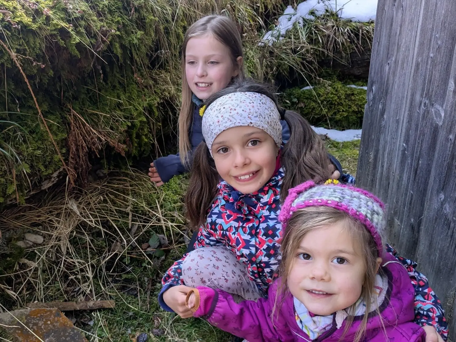 Drei Kinder hocken in winterlicher Waldumgebung auf dem Boden und betrachten etwas im Moos zwischen Gras und Schneeresten. | © DAV Markt Schwaben/Silke Titze