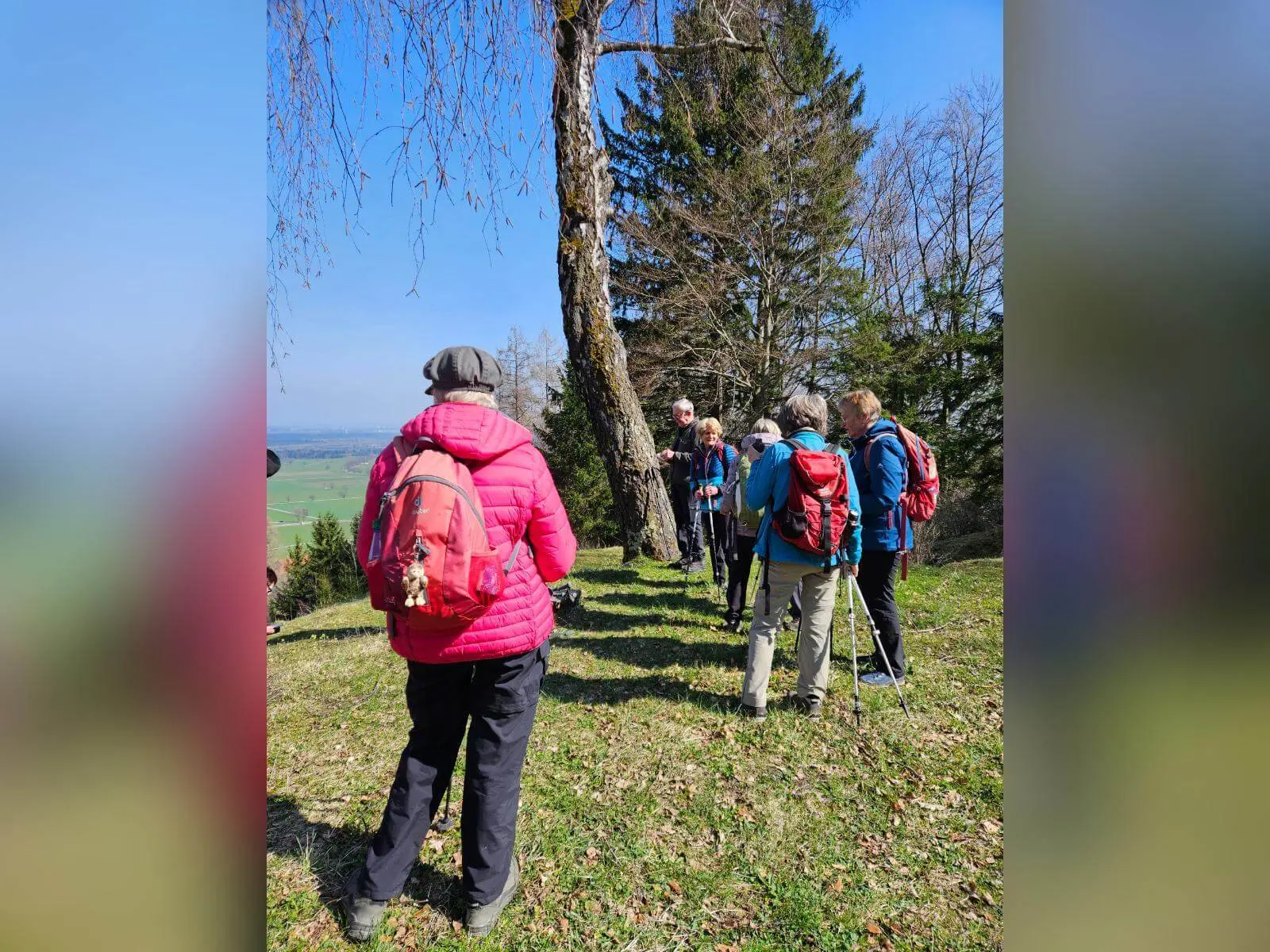 Teilnehmende der Seniorengruppe stehen auf einer sonnigen Wiese mit Wanderstöcken, im Hintergrund Blick ins Tal bei Bad Feilnbach. | © DAV Markt Schwaben