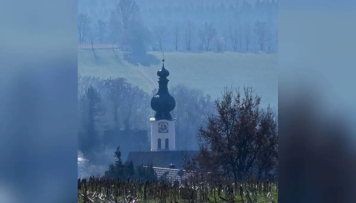 Eine Kirche mit Zwiebelturm steht in einem Tal; vorne ein abgeerntetes Feld, dahinter Hügel und Wald, teils im dunstigen Licht. | © DAV Markt Schwaben/Hubert Inhofer