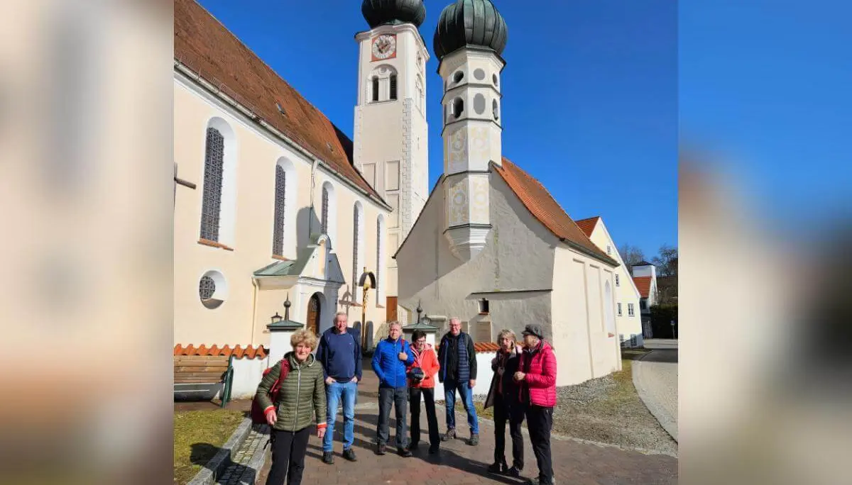 Sieben Wandernde stehen vor der Wallfahrtskirche Maria Himmelfahrt; vorne die Gruppe, daneben ein separates Gebäude, darüber klarer Himmel.  | © DAV Markt Schwaben/Hubert Inhofer