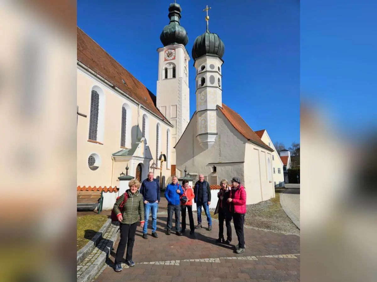 Sieben Wandernde stehen vor der Wallfahrtskirche Maria Himmelfahrt; vorne die Gruppe, daneben ein separates Gebäude, darüber klarer Himmel.  | © DAV Markt Schwaben/Hubert Inhofer