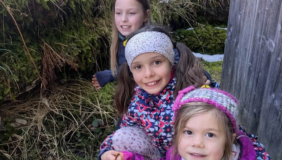 Drei Kinder hocken in winterlicher Waldumgebung auf dem Boden und betrachten etwas im Moos zwischen Gras und Schneeresten. | © DAV Markt Schwaben/Silke Titze