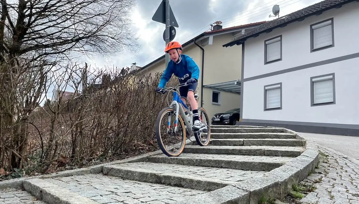 Ein Radfahrer fährt eine gebogene Steintreppe hinab; er trägt Helm und blaue Kleidung, im Hintergrund stehen Wohnhäuser und ein Auto. | © DAV Markt Schwaben/Miron Thoms