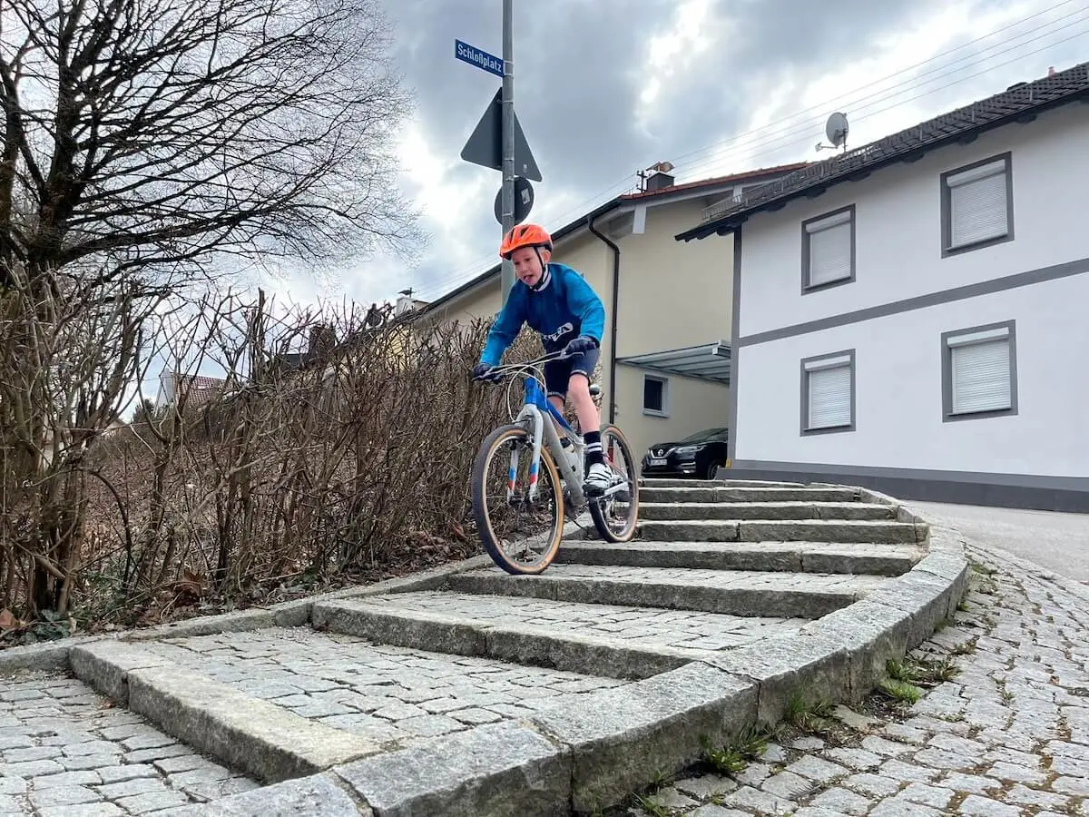 Ein Radfahrer fährt eine gebogene Steintreppe hinab; er trägt Helm und blaue Kleidung, im Hintergrund stehen Wohnhäuser und ein Auto. | © DAV Markt Schwaben/Miron Thoms