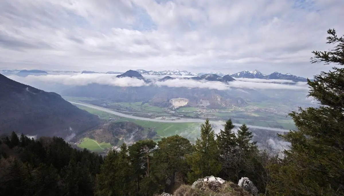 Weitblick vom felsigen Hang über bewaldete Hänge ins Inntal mit Flusslauf, darüber schweben Wolken vor alpiner Bergkulisse. | © DAV Markt Schwaben/Erwin Matzinger