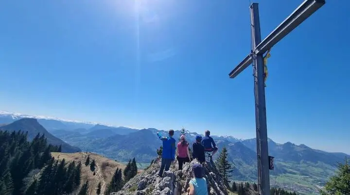 Familiengruppe steht am Gipfelkreuz des Heubergs und blickt über weites Bergpanorama mit Tälern und Gipfeln. | © DAV Markt Schwaben/Maria Wenisch