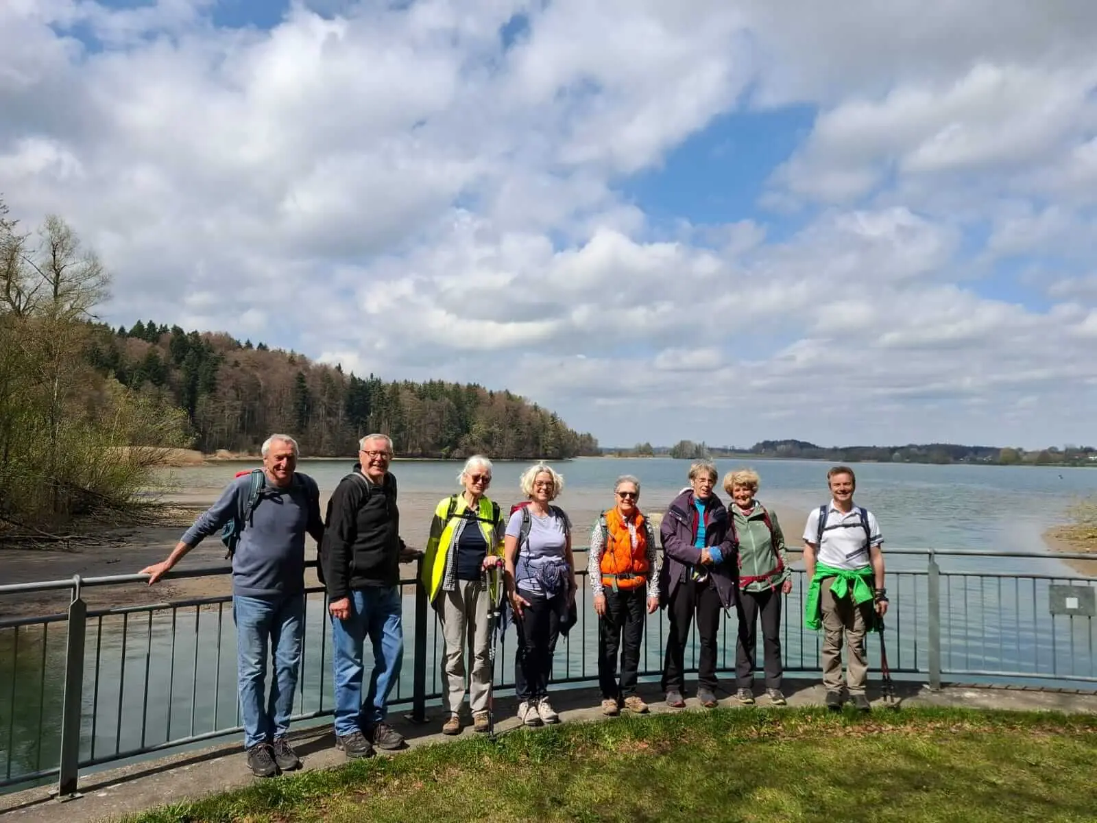 Gruppe älterer Wandernder steht am Ufer des Seehamer Sees vor Geländer und Wasser; im Hintergrund Uferwald und Wolkenhimmel. | © DAV Markt Schwaben/Rudolf Mandausch