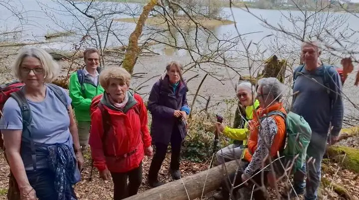 Wandergruppe steht auf schmalem Pfad im lichten Uferwald des Seehamer Sees; im Hintergrund Wasserfläche und gegenüberliegendes Ufer. | © DAV Markt Schwaben/Rudolf Mandausch
