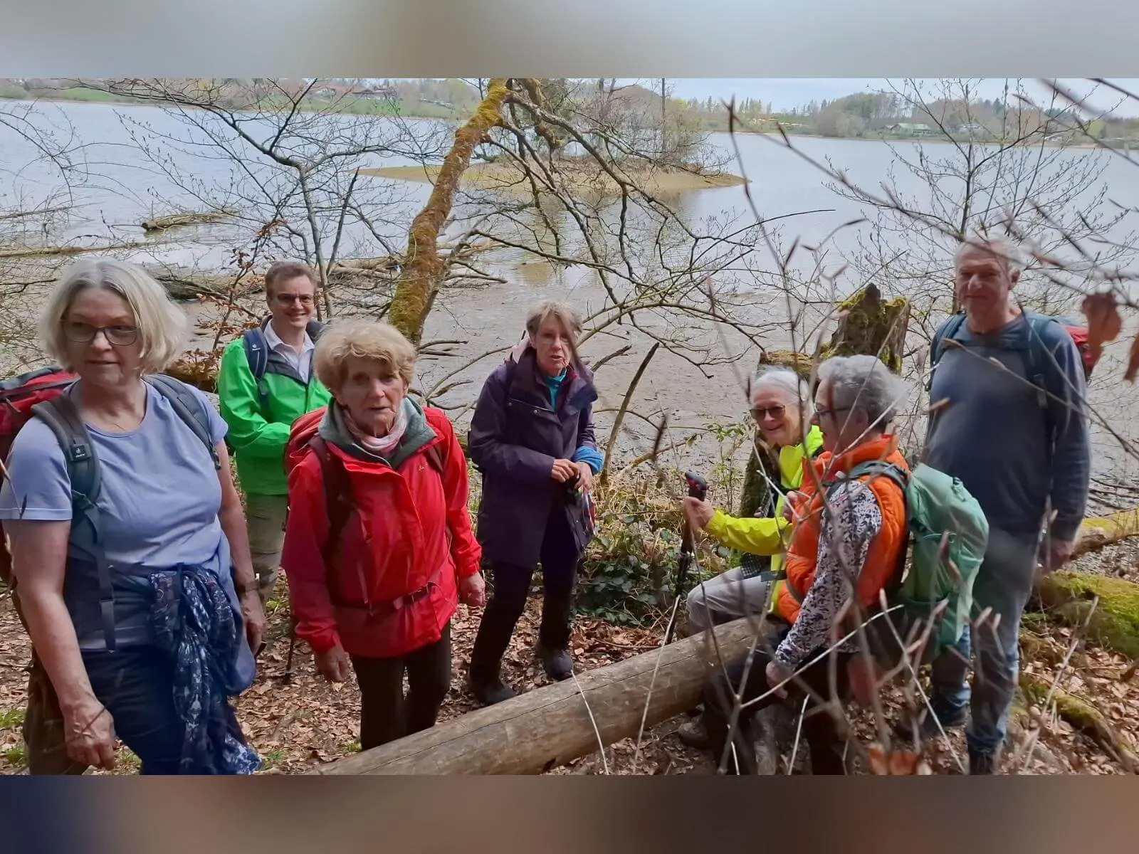 Wandergruppe steht auf schmalem Pfad im lichten Uferwald des Seehamer Sees; im Hintergrund Wasserfläche und gegenüberliegendes Ufer. | © DAV Markt Schwaben/Rudolf Mandausch