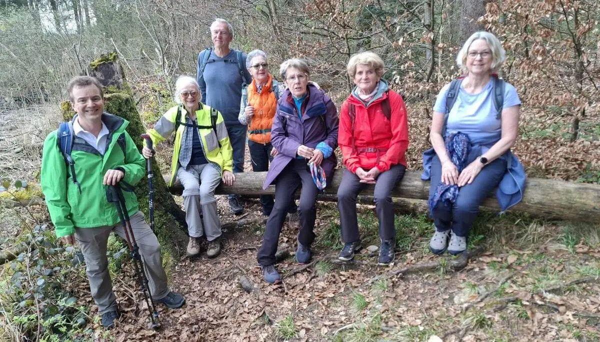 Seniorengruppe sitzt und steht an einem umgestürzten Baumstamm im Wald; Wanderstöcke und Rucksäcke zeigen eine Rast während der Seeumrundung. | © DAV Markt Schwaben/Rudolf Mandausch