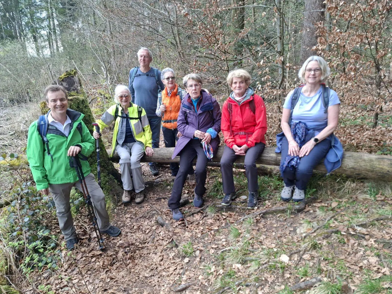 Seniorengruppe sitzt und steht an einem umgestürzten Baumstamm im Wald; Wanderstöcke und Rucksäcke zeigen eine Rast während der Seeumrundung. | © DAV Markt Schwaben/Rudolf Mandausch