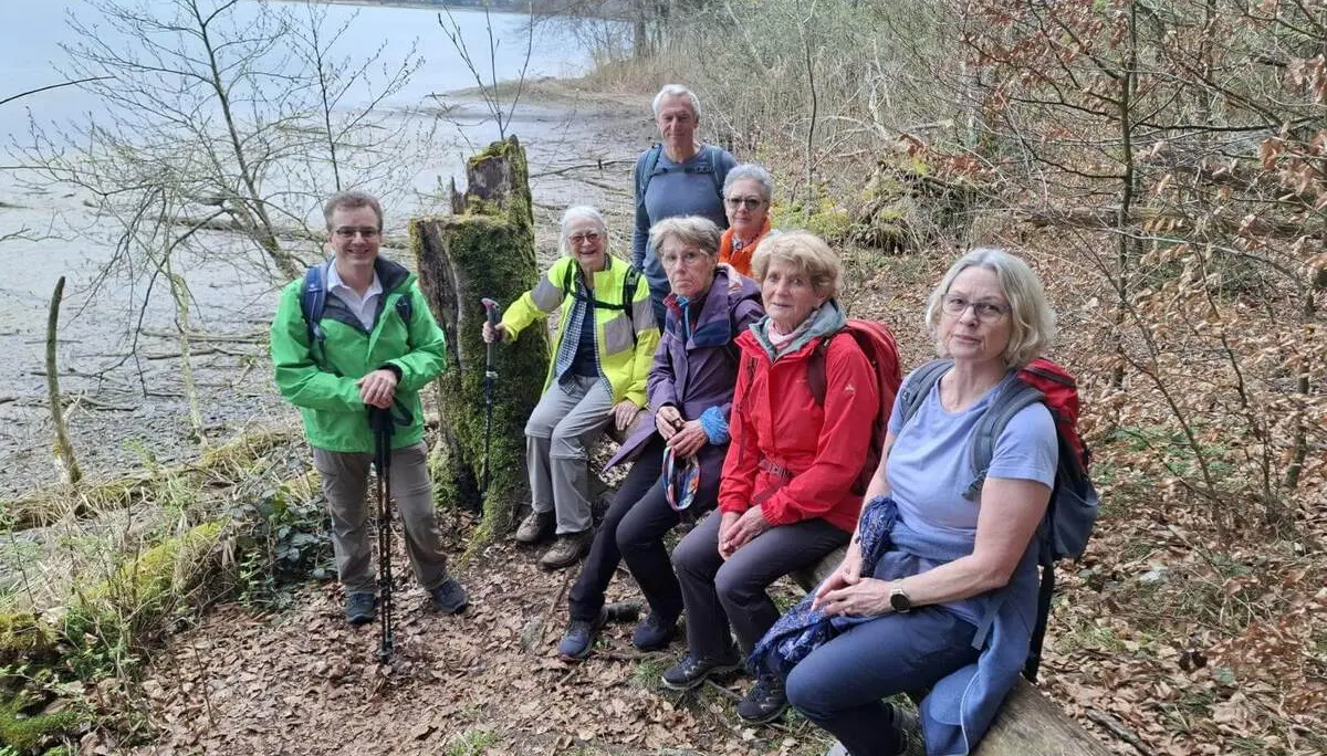 Seniorengruppe macht Pause auf Baumstämmen am Ufer des Seehamer Sees; Wanderstöcke und Rucksäcke liegen bereit, Wasser und Laubwald im Hintergrund. | © DAV Markt Schwaben/Rudolf Mandausch