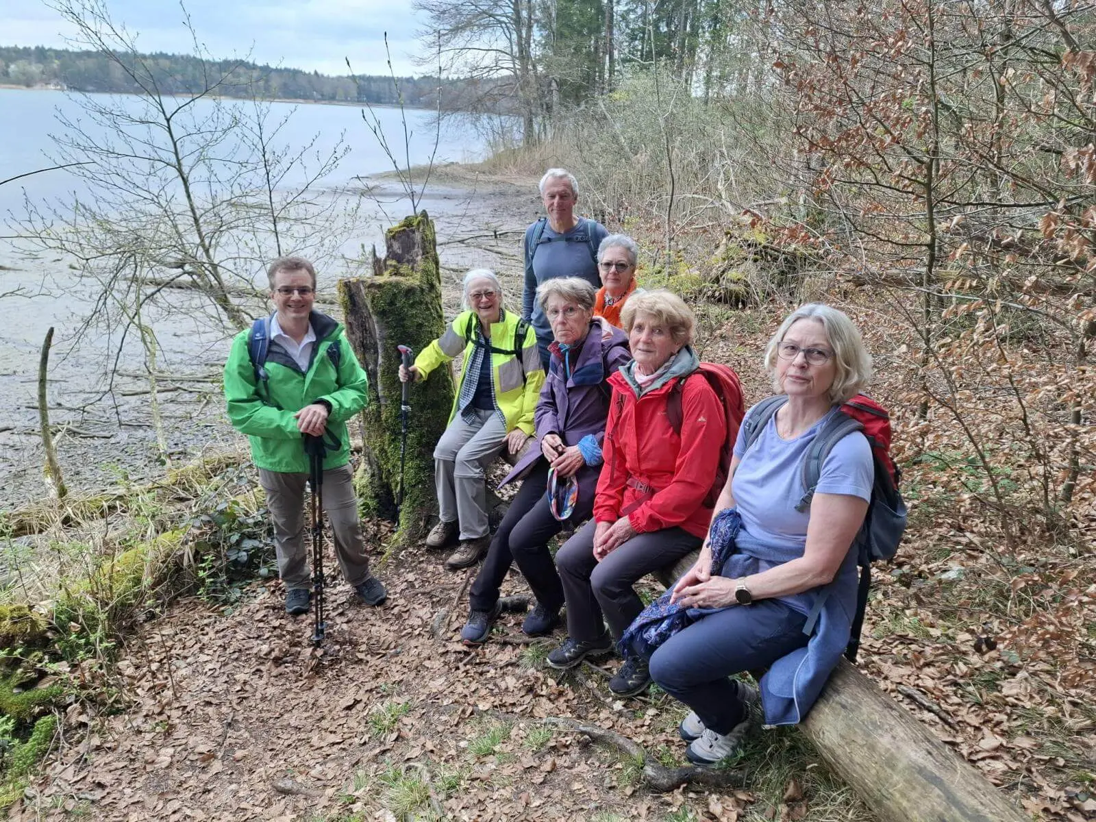 Seniorengruppe macht Pause auf Baumstämmen am Ufer des Seehamer Sees; Wanderstöcke und Rucksäcke liegen bereit, Wasser und Laubwald im Hintergrund. | © DAV Markt Schwaben/Rudolf Mandausch